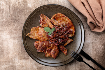 A plate of fried beef liver with caramelized onions and sage.