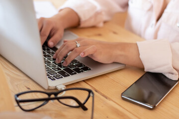 Closeup shot of Caucasian woman typing on laptop keyboard. Young woman in white shirt pressing keys, editing documents or posting content on computer in office. Office work, small business concept