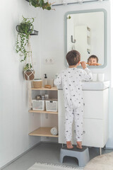 Cute male kid in pajamas cleaning teeth with eco friendly toothbrush comfortable minimalist bathroom