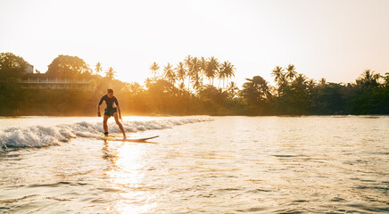 Teen boy silhouette riding a long surfboard. He caught a wave in an Indian ocean bay with magic...