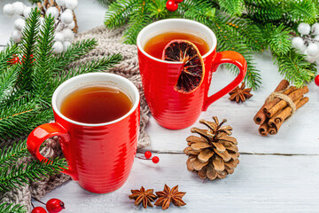 Hot winter or Christmas tea in ceramic red cups. Fir tree branches, lemon slice, spices and berries