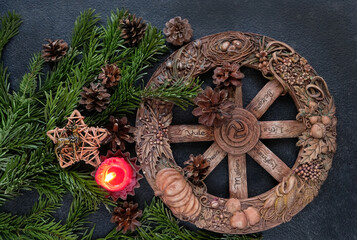 wiccan altar with Wheel of the year candle, amulet deer, cones, fir branches on dark abstract...
