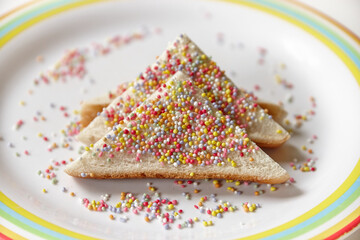 horizontal close up shot of a pair of fairy bread on a white plate with colorful border design