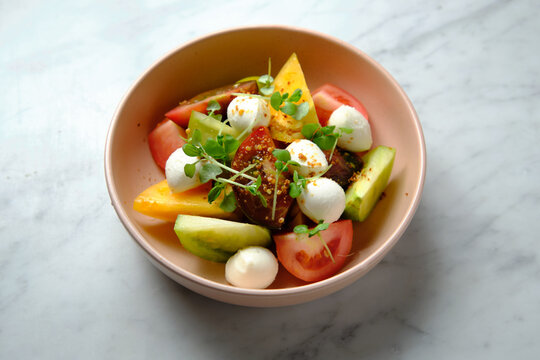 Top shot of heirloom tomatoes salad with mozzarella cheese in a pink bowl