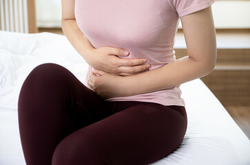 Woman suffering from stomachache is sitting on the bed and clutching her stomach 