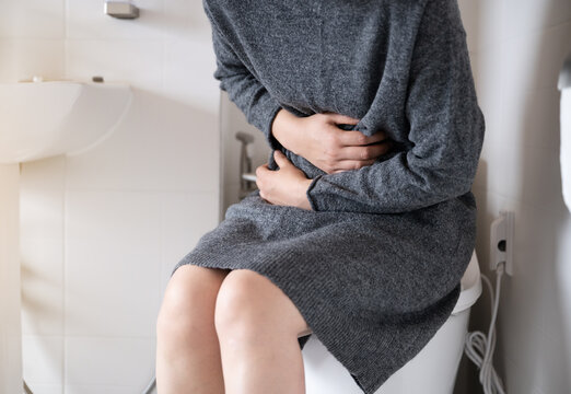 A woman suffering from stomach pain is sitting on the toilet and clutching her stomach