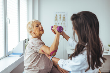 Female physiotherapists provide assistance to senior female patients with elbow injuries examine...