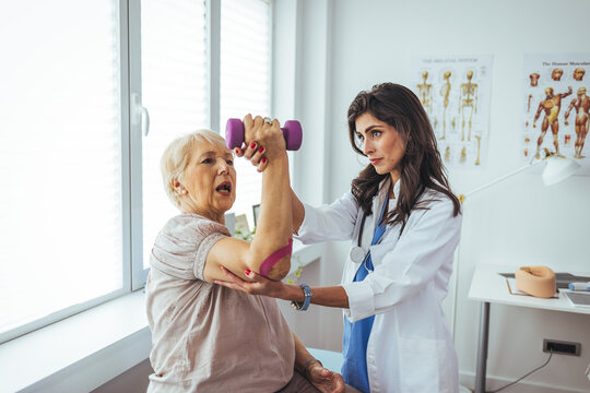 Senior woman is experiencing pain in her elbow. A female doctor is examining the woman's arm. Problem is at the elbow. Physiotherapist working with patient. 
