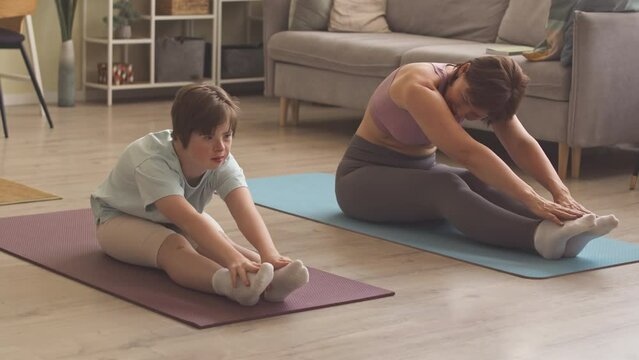 14 year old Caucasian girl with down syndrome and her mother stretching on mats while exercising at home