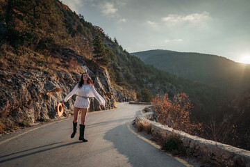 The woman is dear to the mountains. A woman in a white sweater, black boots and a hat walks along a winding alpine path between the mountains at the end of summer at sunset. Travel concept.