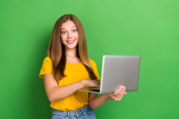 Photo of positive smiling brown hair teenager girl wear orange t-shirt hold laptop browsing useful information isolated on green color background