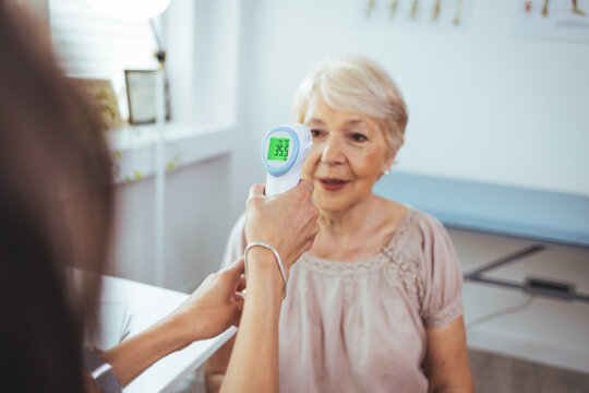 Medical Doctor Checking Senior Patient Temperature With Infrared Thermometer. Receptionist Checking Fever Middle Age Woman By Digital Thermometer For Fever Scan. Healthcare Concept