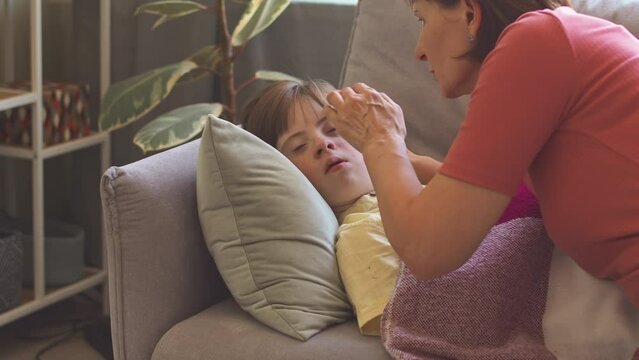 Caring mother taking care of her daughter with down syndrome napping on couch in living room