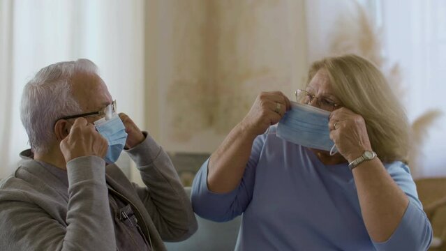 Medium shot of mature couple putting on protective masks at home. Senior man and woman taking care of their health during self-isolation, wearing virus protection masks. Retirement, pandemic concept