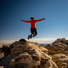 Woman In Orange Jacket Jumps On Top of HIgh Rocks