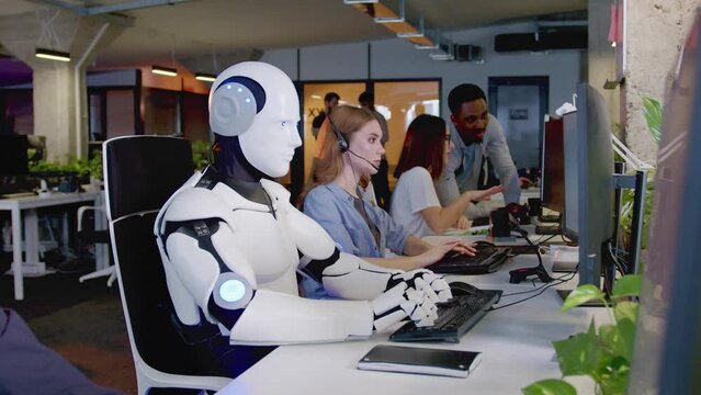 Side-view portrait futuristic white robot with artificial intelligence working in crowded office typing on keyboard using computer. Smart cyborg working with people in IT company. Technologies concept