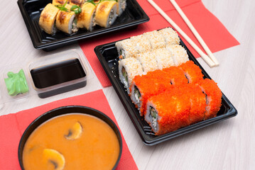Delicious Japanese rolls with salmon, avocado, cucumber, cheese, tom yum soup in takeout packaging with wood sticks and soy sauce. Selective focus. Asian food and delivery concept. Healthy eating