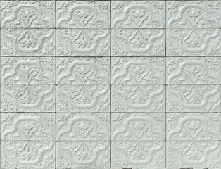 Zócalo de una casa española con motivos decorativos florales de patrón. Fondo de azulejos de cerámica en relieve pintados de gris. Composición de losetas cerámicas para decoración de fachada