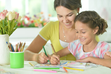 little girl with mother drawing at the table at home