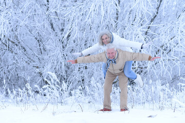 elderly man holding an old woman on his back in winter