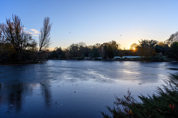 A frozen lake at sunset. There is ice on the surface of the lake in this winter scene. A cold winter's day in Kelsey Park, Beckenham, Kent, UK.