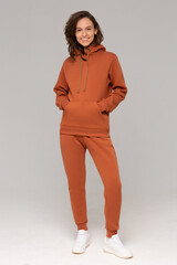 Smiling woman with thick curly hair in a brown suit of hoodies and sweatpants. Mock-up.
