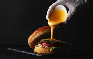Hand pouring  melted cheese sauce on Homemade beef  burger on  black plate  - Powered by Adobe