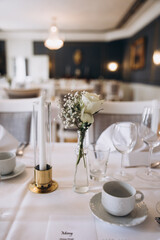 Wedding. Banquet. On festive tables with white tablecloths there are compositions of flowers, candles, cutlery, glasses, plates, menu cards and name plates