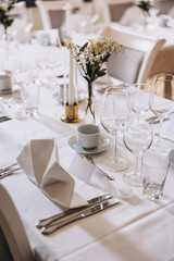 Wedding. Banquet. On festive tables with white tablecloths there are compositions of flowers, candles, cutlery, glasses, plates, menu cards and name plates