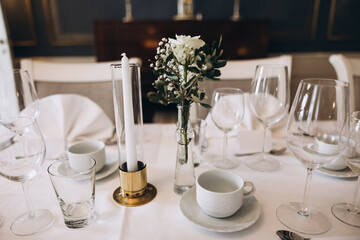 Wedding. Banquet. On festive tables with white tablecloths there are compositions of flowers, candles, cutlery, glasses, plates, menu cards and name plates
