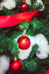 Red Christmas balls and red bow ribbon adorn on Christmas tree.  Christmas background and bokeh. New Year concept.