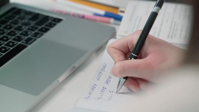 Girl Takes Notes on Notebook from Her Laptop. Close-up of Women's Hands Writing with Pen in Paper Notebook