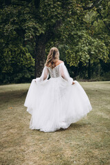 Fototapeta na wymiar Wedding. A bride in a white dress walks along the green grass against the background of trees