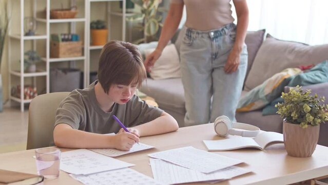 Mother helping teenage daughter with down syndrome with home assignment