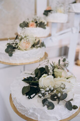 Wedding. Banquet. A cake for the bride and groom stands on a table with a white tablecloth, candles stand nearby and is decorated with flowers and greenery. Nearby are candles, plates and cutlery