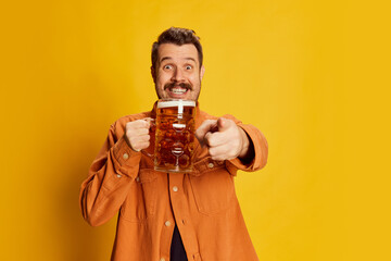 Portrait of emotive happy man in orange shirt posing with lager foamy beer glass isolated over...