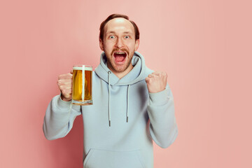 Portrait of young man, sport fan with excited happy look posing with lager foamy beer mug isolated...