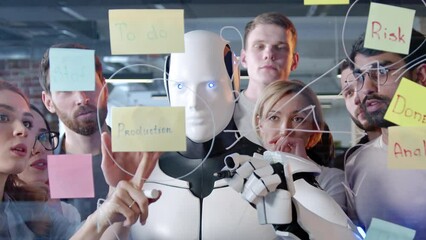 Close-up portrait of futuristic modern robot working with multiethnic people brainstorming ideas for app writing on glass board in office. Professional smart employees with AI cyborg.