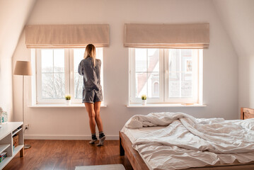 Fototapeta na wymiar Young woman stands near the window on a sunny morning. Morning exercise and meditation. Awakening from sleep. Good morning magic morning. Women's recreation
