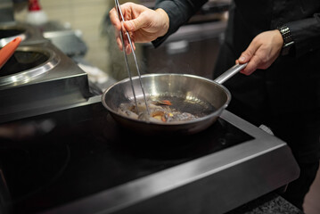man chef cooking tasty shrimp in frying pan on kitchen