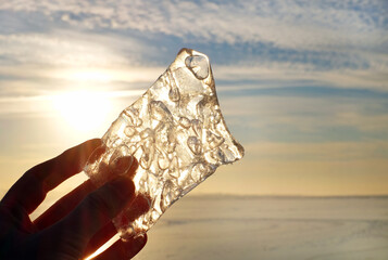 Piece of ice in hand, winter landscape in sunny day