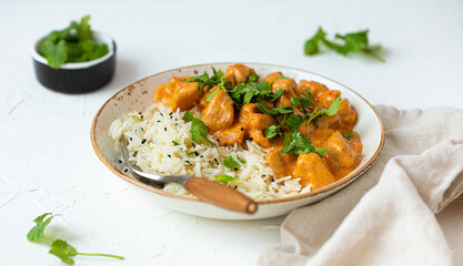 Traditional Indian dish chicken curry with basmati rice and fresh cilantro on rustic white plate on white concrete kitchen table, close up with selective focus. Indian dinner meal