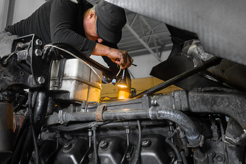 Car mechanic repairs large truck or tractor in workshop. Professional mechanic repairs truck engine. Genuine worker..
