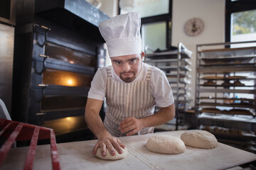 Young baker with down syndrome preparing pastries in bakery. Concept of integration people with disabilities into society.
