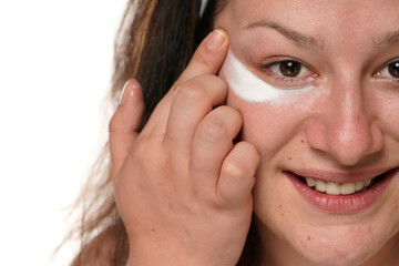 portrait of a young smiling woman chubby applying cosmetic product under her eyes on a white background.