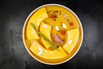 Seasoned pieces of fresh pumpkin with spices and on a round orange plate on black table, vegan pumpkin
