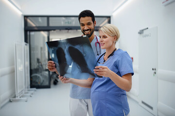 Pregnant doctor checking x-ray image with her colleague at hospital corridor.