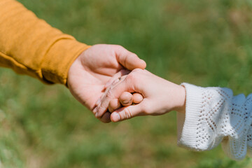 The hands of a man and a woman hold each other against the background of green grass on a bright sunny day, white and yellow clothes, the concept of peace, mutual assistance, friendship, harmony
