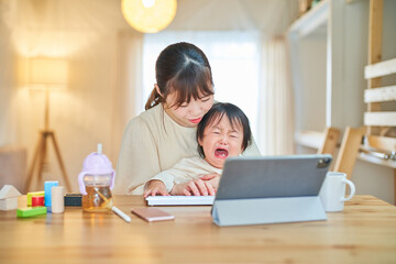 Fototapeta na wymiar 疲れた表情で自宅でタブレットPCを操作する女性と幼児