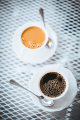 two white cups of coffee with spoons on a white table outside